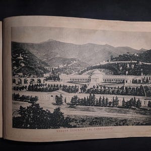 May include: A black and white photograph of a cemetery in a mountainous region. The photo shows a large, open area with a building in the center and rows of trees surrounding it. The text "VEDUTA GENERALE DEL CAMPOSANTO" is printed at the bottom of the photo.