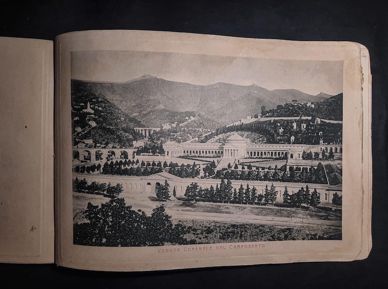 May include: A black and white photograph of a cemetery in a mountainous region. The photo shows a large, open area with a building in the center and rows of trees surrounding it. The text "VEDUTA GENERALE DEL CAMPOSANTO" is printed at the bottom of the photo.
