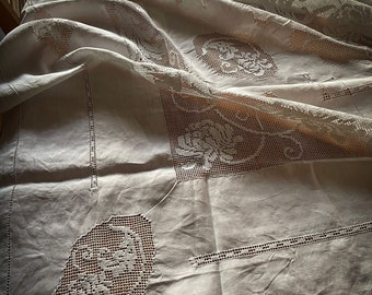 May include: A white crocheted tablecloth with intricate floral designs. The tablecloth is draped over a table and has a delicate, lacy texture.