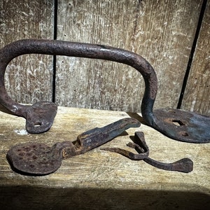 May include: A set of four antique rusty metal door hardware pieces, including a handle, a latch, a keyhole cover, and a hook. The pieces are arranged on a wooden surface.