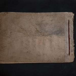 May include: A worn, tan-colored book cover with a brown string sewn along the spine.
