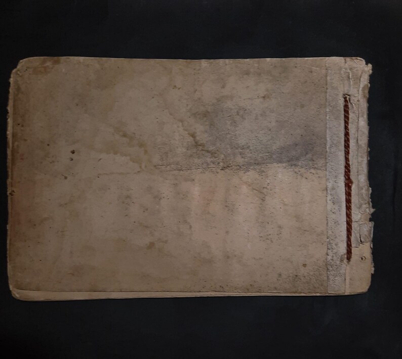 May include: A worn, tan-colored book cover with a brown string sewn along the spine.