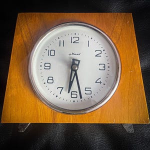 May include: A vintage Max alarm clock with a light brown wooden frame and a white clock face. The clock face has black numerals and hands, with a silver-colored bezel. The clock is set to approximately 6:30.