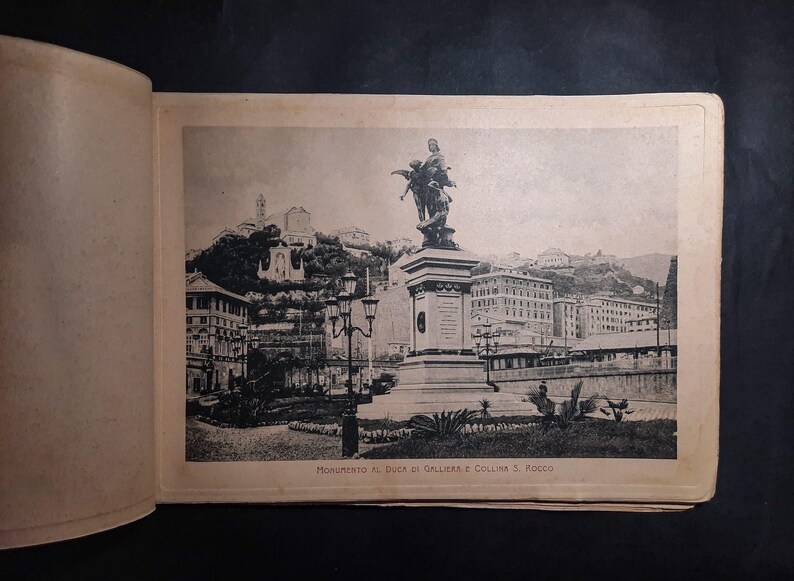 May include: A black and white photo of a monument to the Duke of Galliera and the hill of Rocca. The monument is a statue of a man on horseback, and it is located in a city setting. The photo is from an old postcard.