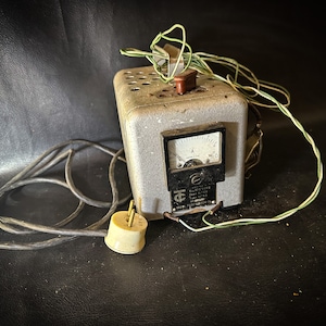 Könnte beinhalten: Ein altes, graues elektrisches Gerät aus Metall mit einem schwarzen Zifferblatt und einem weißen Stecker. Das Gerät hat ein grünes Kabel.