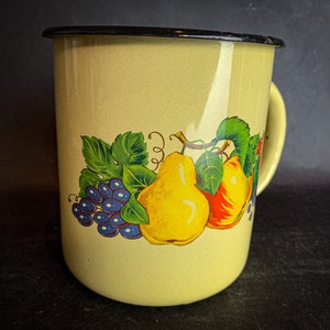 May include: A yellow enamel mug with a black rim and handle. The mug features a colorful illustration of pears, grapes, and leaves.