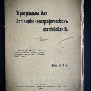Può includere: Una copertina di libro vintage con testo russo, con il titolo "Programmi per la ricerca botanica e geografica". La copertina è di colore beige sbiadito con testo nero e una piccola illustrazione. Il libro è del 1910.