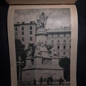 May include: A black and white photograph of a monument to Christopher Columbus in La Paz, Bolivia. The monument features a statue of Columbus standing on a pedestal with other figures surrounding him. The text "A Cristoforo Colombo La Pazia" is visible on the monument.