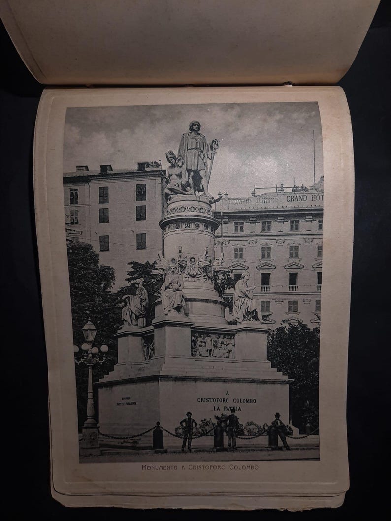 May include: A black and white photograph of a monument to Christopher Columbus in La Paz, Bolivia. The monument features a statue of Columbus standing on a pedestal with other figures surrounding him. The text "A Cristoforo Colombo La Pazia" is visible on the monument.