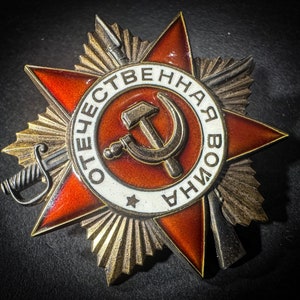 May include: A gold and red metal medal with a star and the words "ОТЕЧЕСТВЕННАЯ ВОЙНА" in a circle around a hammer and sickle.
