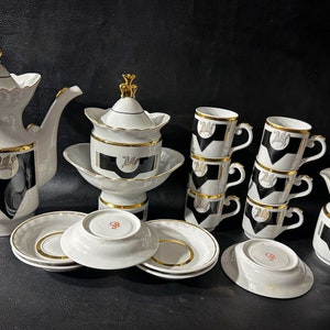 May include: A black and white porcelain tea set with gold accents. The set includes a teapot, sugar bowl, creamer, six cups, and six saucers.
