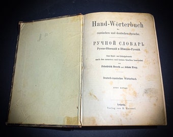 Op de afbeelding: De omslag van een vintage Duits-Russisch woordenboek met de titel "Hand-Wörterbuch" en "РУЧНОЙ СЛОВАРЬ". Het boek is gebonden in bruin leer en heeft een vergeelde, verouderde papieren omslag. De titelpagina bevat de tekst "Zum land- und Schalgebraach nach den neuesten und besten Quellen bearbeitet von Friedrich Booch und Adam Frey." Het boek is een achtste editie en werd uitgegeven in Leipzig door H. Hasssel.