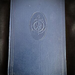 May include: A navy blue hardcover book with a raised embossed image of an anchor and compass on the front cover.