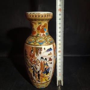 Op de afbeelding: Een keramische vaas met een gouden en witte achtergrond en een kleurrijk bloemenontwerp met Japanse vrouwen. De vaas is ongeveer 50 cm hoog.