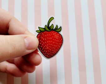 May include: A die-cut sticker featuring a vibrant red strawberry with small white seeds and a green leafy stem at the top. The illustration has a clean white border around the edges, highlighting the bright red color of the fruit.