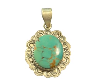 May include: A silver pendant with a large, oval turquoise stone. The stone is a vibrant turquoise color with brown veining. The pendant has a decorative, scalloped silver border and a silver loop for a chain.