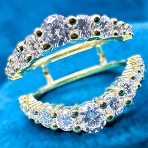 May include: A pair of gold-toned earrings with a double-hoop design. Each hoop is encrusted with multiple round, clear gemstones. The earrings are set against a blue background, highlighting the sparkle of the stones.