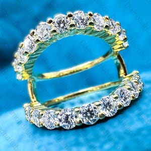 May include: A pair of gold hoop earrings with a row of sparkling white gemstones. The earrings are set against a vibrant blue background, showcasing the jewelry's brilliance. The design is elegant and classic.