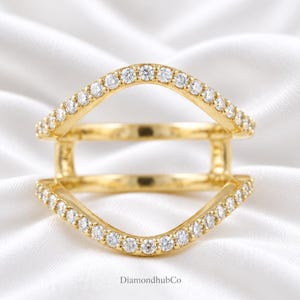 May include: A gold double-band ring featuring two arched, open-work bands connected by vertical bars. Both bands are pavé-set with small, clear, round-cut stones along the outer edges. The text DiamondhubCo is printed at the bottom of the image.