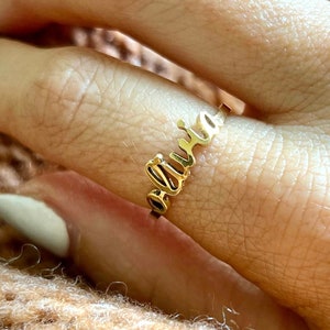 May include: A gold ring with the name "Olivia" spelled out in cursive lettering.