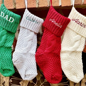 May include: Four knitted Christmas stockings with personalized names: Dad, Gabriel, Amelia, and Aaron. The stockings are green, white, red, and cream.