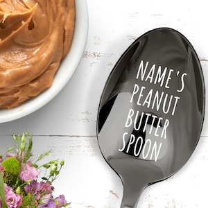 May include: A black personalized spoon with the text "NAME'S PEANUT BUTTER SPOON".
