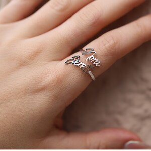 May include: A silver ring with the names "Mom" and "Forever" engraved on it. The ring is worn on a finger.