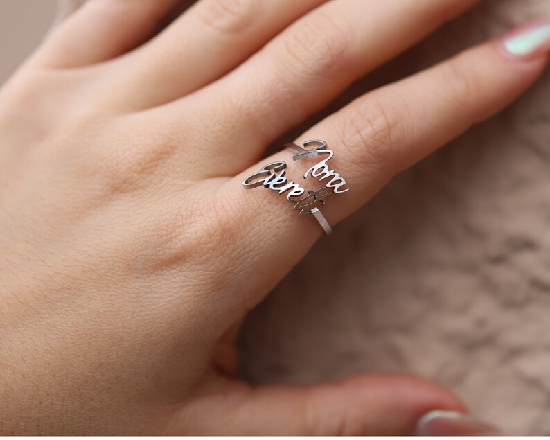May include: A silver ring with the names "Mom" and "Forever" engraved on it. The ring is worn on a finger.
