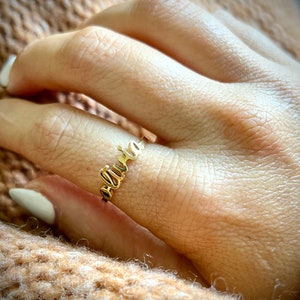 May include: A gold ring with the name "Olivia" spelled out in cursive lettering.