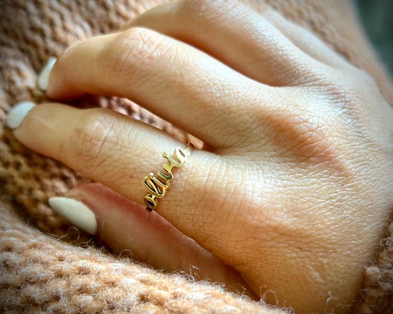 May include: A gold ring with the name "Olivia" spelled out in cursive lettering.