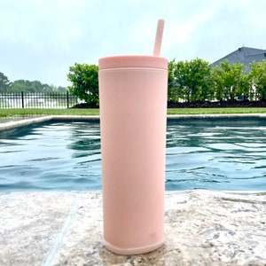 May include: A pink stainless steel tumbler with a straw, sitting by a swimming pool.