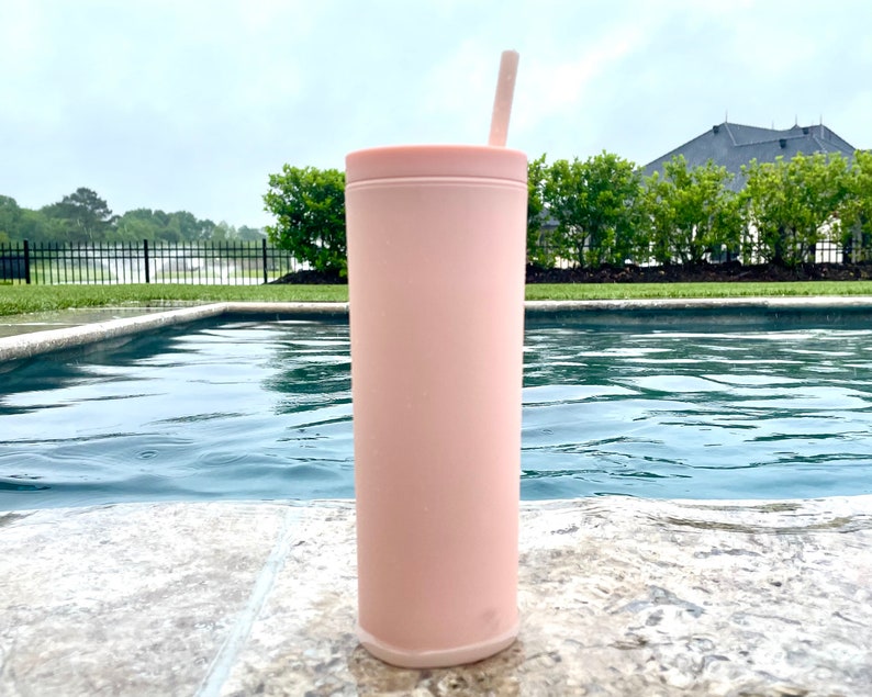 May include: A pink stainless steel tumbler with a straw, sitting by a swimming pool.