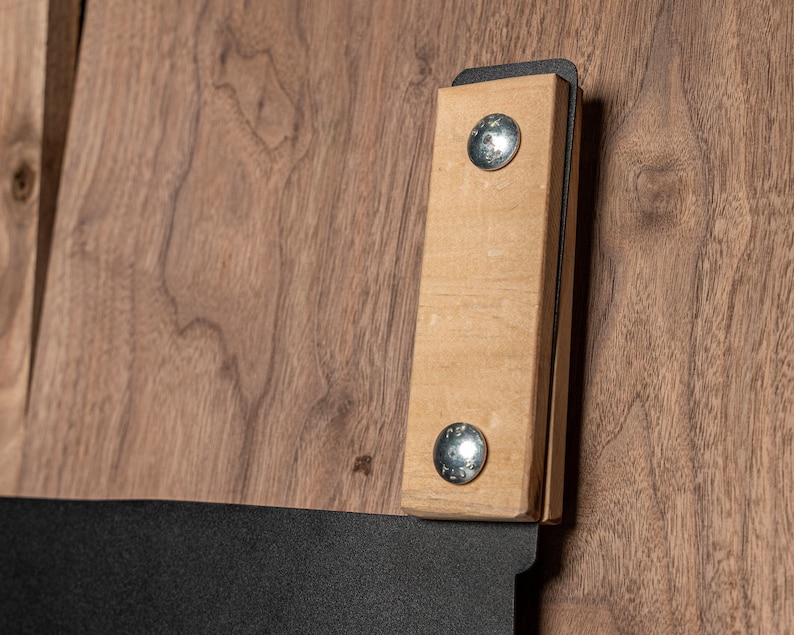 Puede incluir: Primer plano de un mango de madera con dos tornillos plateados unidos a un marco de metal negro. El mango es de madera marr&oacute;n claro y tiene una superficie lisa.