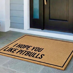 K&ouml;nnte beinhalten: Eine rechteckige Fu&szlig;matte aus Naturfasern mit schwarzem Rand. Die Matte zeigt den Text "I HOPE YOU LIKE PITBULLS" in fetten, schwarzen Buchstaben und hei&szlig;t die G&auml;ste willkommen.