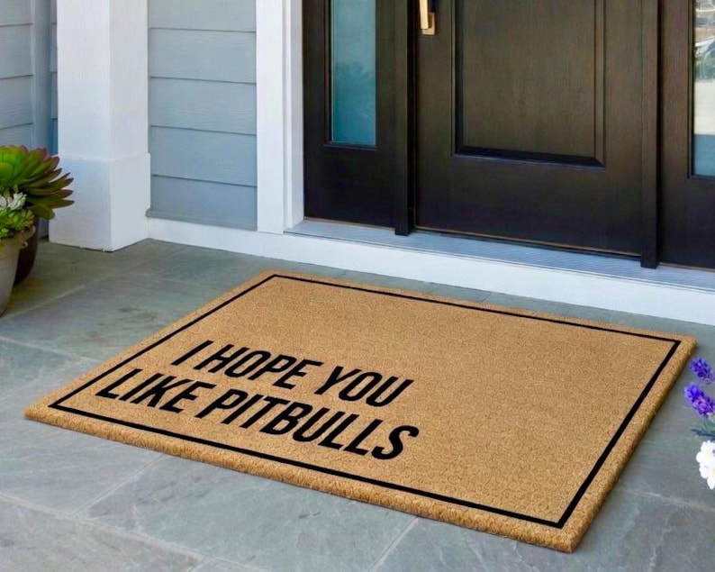 K&ouml;nnte beinhalten: Eine rechteckige Fu&szlig;matte aus Naturfasern mit schwarzem Rand. Die Matte zeigt den Text "I HOPE YOU LIKE PITBULLS" in fetten, schwarzen Buchstaben und hei&szlig;t die G&auml;ste willkommen.