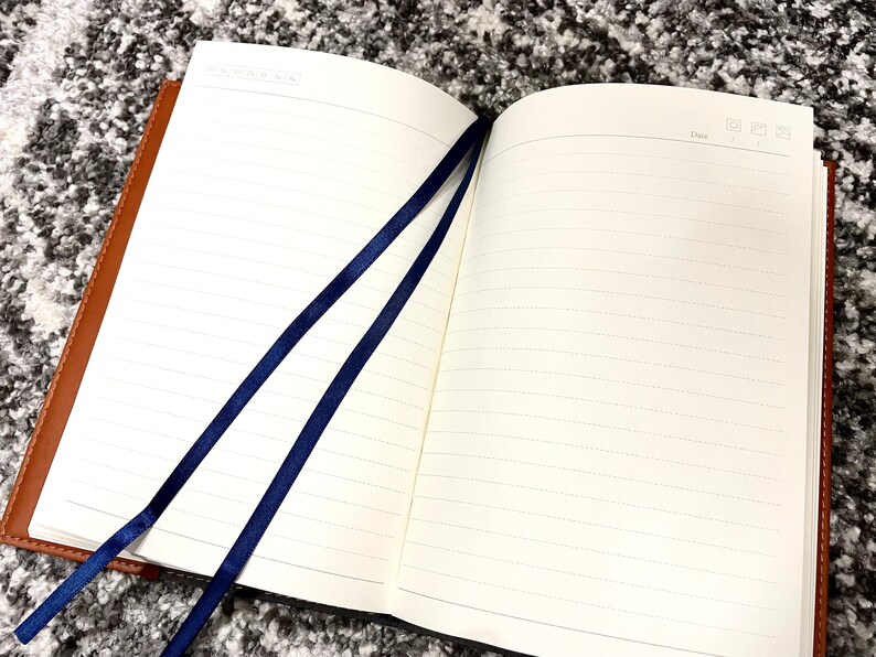 May include: A brown leather-bound journal with two blue ribbon bookmarks. The journal has lined pages and a space for the date at the top of each page.