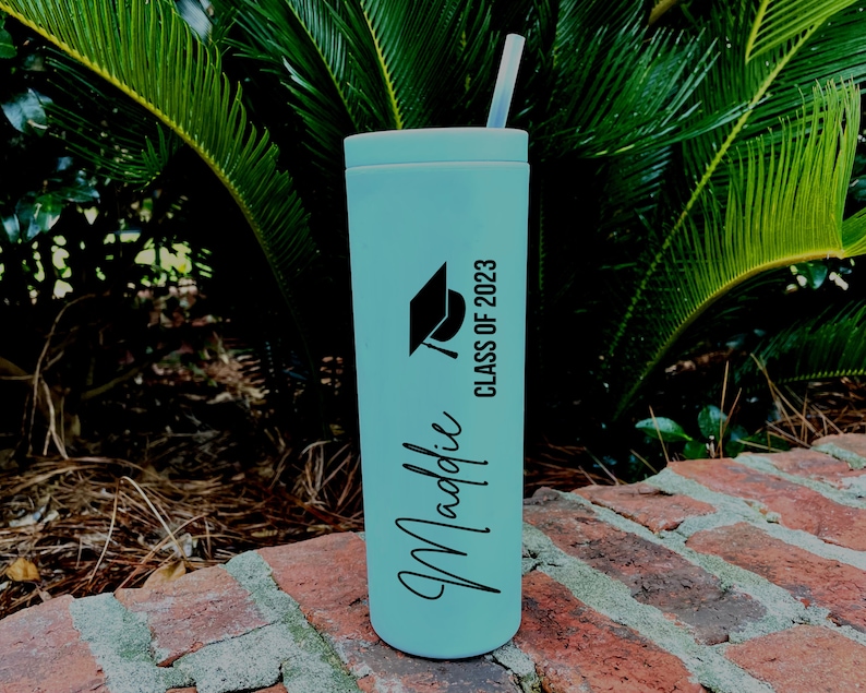 Puede incluir: Un vaso de acero inoxidable azul claro con un gorro de graduaci&oacute;n negro y el texto "Class of 2023". El nombre "Maddie" est&aacute; escrito en cursiva en el vaso.
