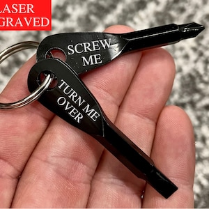 May include: A black metal keychain with two screwdriver heads. The keychain has the text "Screw Me" and "Turn Me Over" engraved on it.