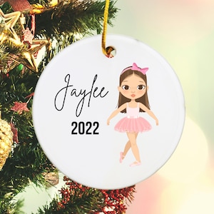 May include: White ceramic Christmas ornament with a cartoon ballerina in a pink tutu and a pink bow in her hair. The ornament has the name "Jaylee" and the year "2022" written on it.