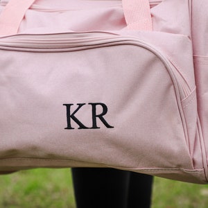 Pu&ograve; includere: Borsa da viaggio in tela rosa con le iniziali "KR" ricamate in nero e una cerniera con un'etichetta "DALIX" argentata.