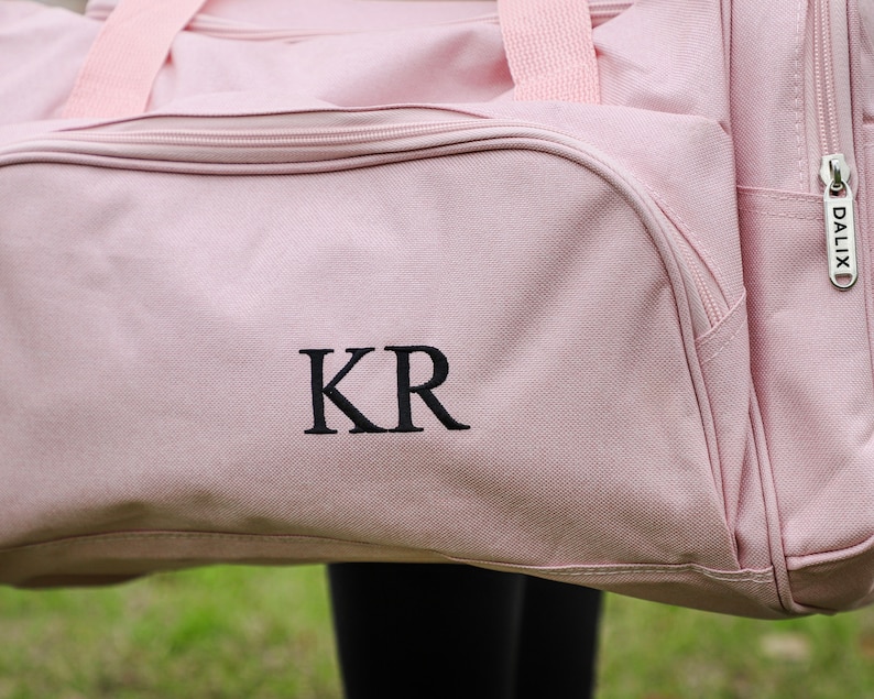 Pu&ograve; includere: Borsa da viaggio in tela rosa con le iniziali "KR" ricamate in nero e una cerniera con un'etichetta "DALIX" argentata.
