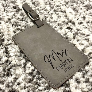 Peut inclure: Etiquette &agrave; bagages en cuir gris avec le texte "Mrs. MARTIN 10.8.21" en noir.
