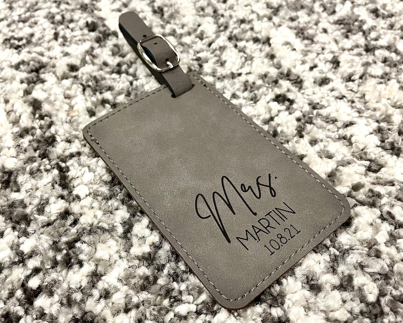 Peut inclure: Etiquette &agrave; bagages en cuir gris avec le texte "Mrs. MARTIN 10.8.21" en noir.