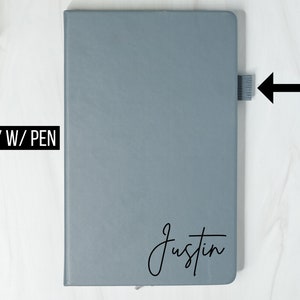 May include: Gray notebook with a black pen loop on the side. The notebook has the name "Justin" written on the front in black cursive.