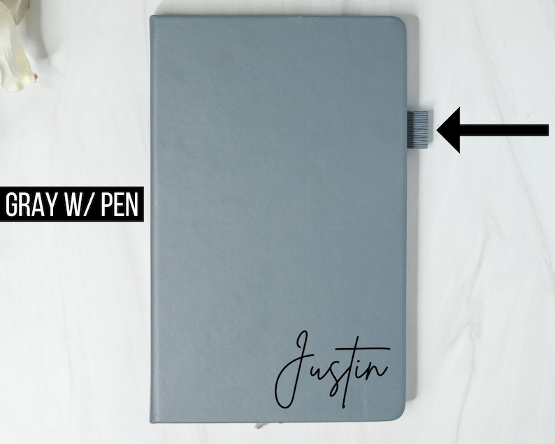 May include: Gray notebook with a black pen loop on the side. The notebook has the name "Justin" written on the front in black cursive.