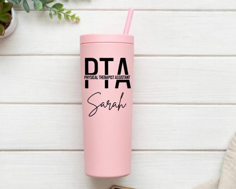 Puede incluir: Un vaso rosa con tapa y pajita a juego. El vaso presenta el texto "PTA PHYSICAL THERAPIST ASSISTANT" en letras negras, con el nombre "Sarah" en escritura cursiva debajo.