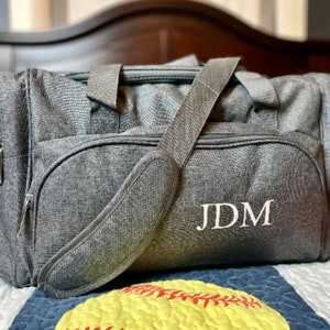 May include: A gray travel duffel bag with a white monogram that reads "JDM".