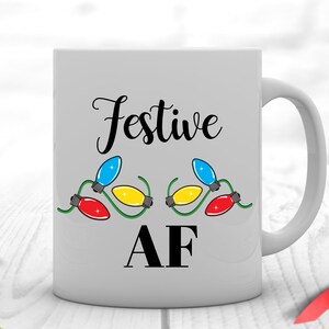 May include: White ceramic mug with a black design that says "Festive AF" with a string of colorful Christmas lights on either side of the text.