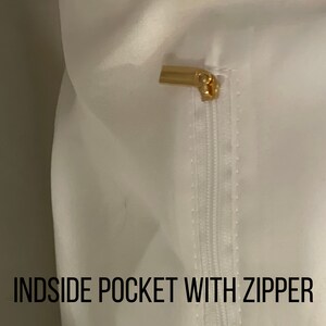 May include: White fabric with a zippered pocket. The zipper pull is gold metal.