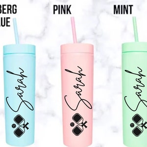 K&ouml;nnte beinhalten: Drei personalisierte Becher mit einem Pickleball-Design. Die Becher sind in den Farben Eisblau, Pink und Mint. Jeder Becher tr&auml;gt den Namen "Sarah" aufgedruckt.